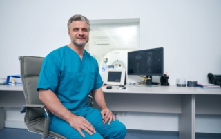 Lekarz w niebieskim fartuchu siedzi przy biurku, co sugeruje, że jest to dobry urolog.